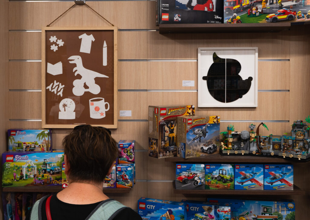 Vue de l'édition 2024 de l'Art en vitrine. Une participante d'une des balade commentée regarde les oeuvres installées à la boutique Le Monde en jeux.